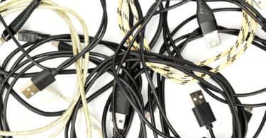 Enchevêtrement de vieux câbles de chargement USB-C, Micro-USB et Lightning, certains noirs et d'autres tressés en nylon jaune, illustrant le stock de câbles inutilisés à recycler ou à détourner.