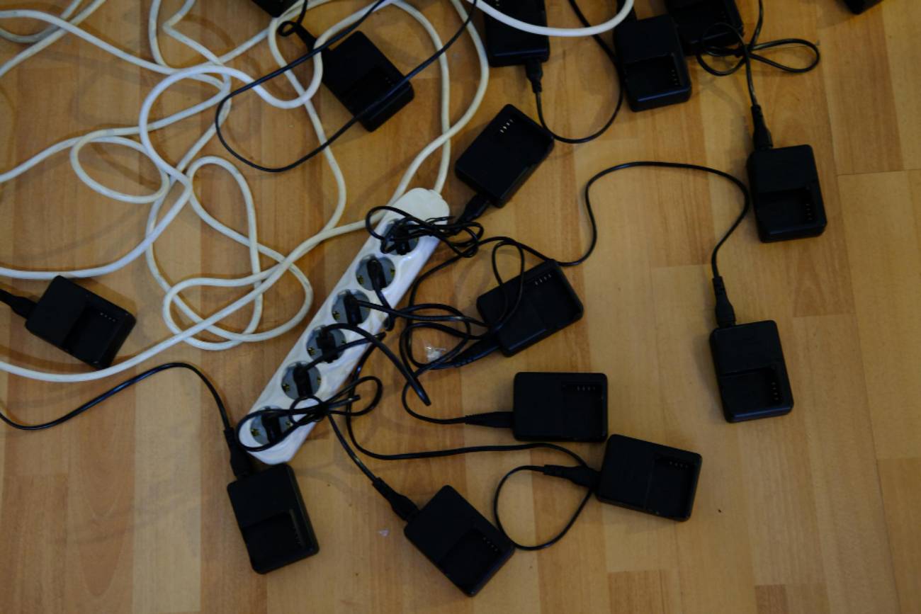 Multiples chargeurs noirs et câbles emmêlés branchés sur une multiprise blanche posée sur un sol en bois, illustrant l'accumulation de déchets électroniques à recycler.
