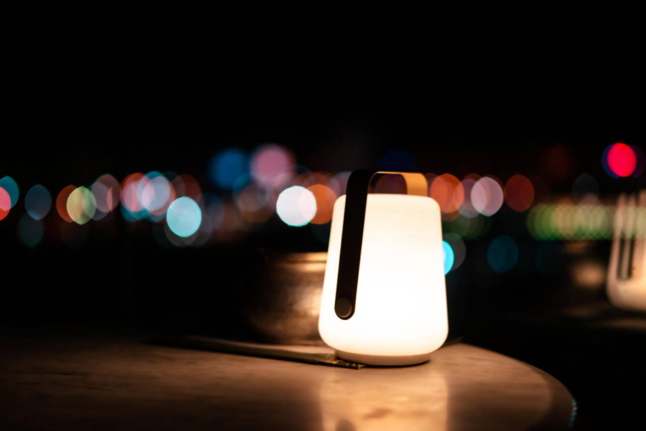 Petite lampe d'appoint artisanale diffusant une lumière chaude et tamisée sur une table, avec un arrière-plan urbain flou (bokeh), illustrant le résultat d'un projet DIY avec des LED et un vieux câble USB.