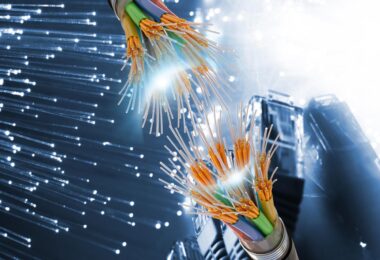 Vue rapprochée de fibres optiques multicolores sectionnées montrant le cœur en verre et les gaines de protection sur un fond numérique bleu.
