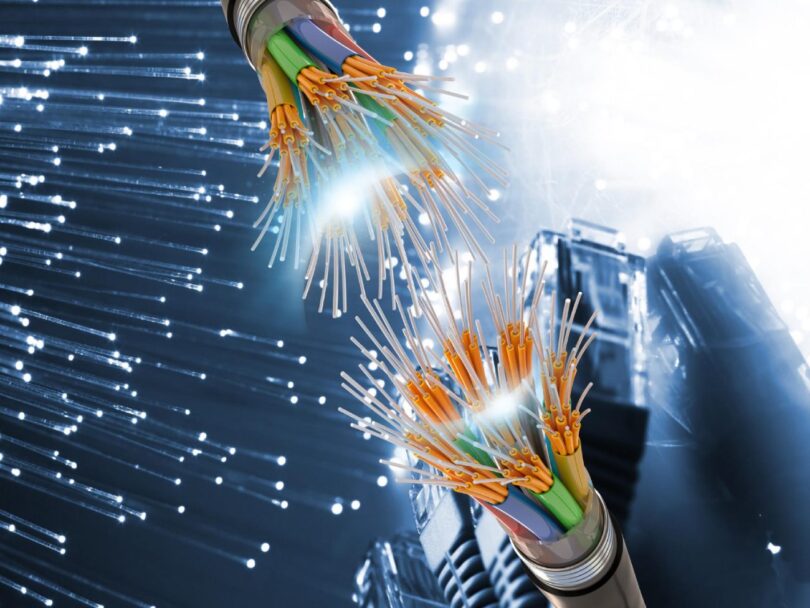 Vue rapprochée de fibres optiques multicolores sectionnées montrant le cœur en verre et les gaines de protection sur un fond numérique bleu.