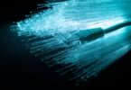 Gros plan artistique d'un connecteur RJ45 sur un fond de fibres optiques lumineuses bleu turquoise illustrant la bande passante et la transmission de données.