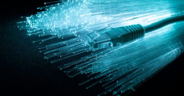 Gros plan artistique d'un connecteur RJ45 sur un fond de fibres optiques lumineuses bleu turquoise illustrant la bande passante et la transmission de données.